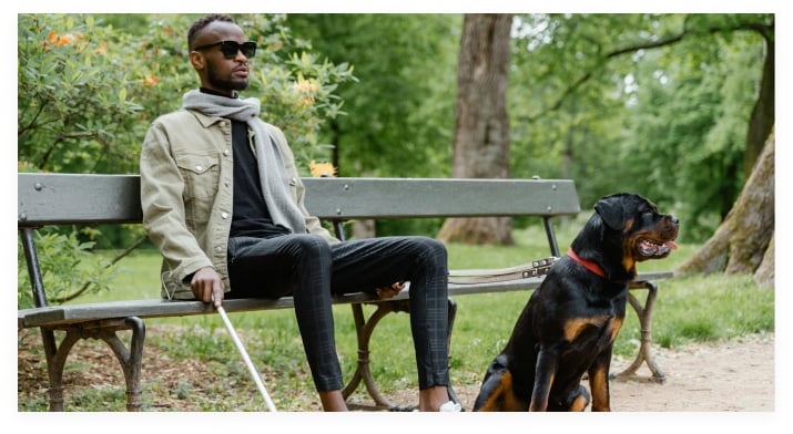 Man with visual impairment sat on park bench with dog
