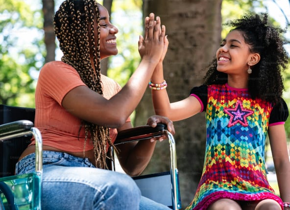 Women in wheelchair high-fiving young girl